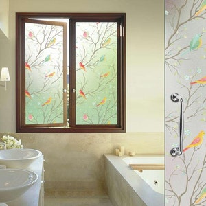 May include: A bathroom window with a frosted glass film featuring a colorful bird and branch design. The film provides privacy while still allowing natural light to enter the room.