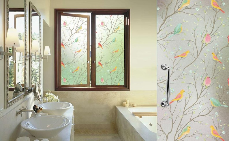 May include: A bathroom window with a frosted glass film featuring a colorful bird and branch design. The film provides privacy while still allowing natural light to enter the room.
