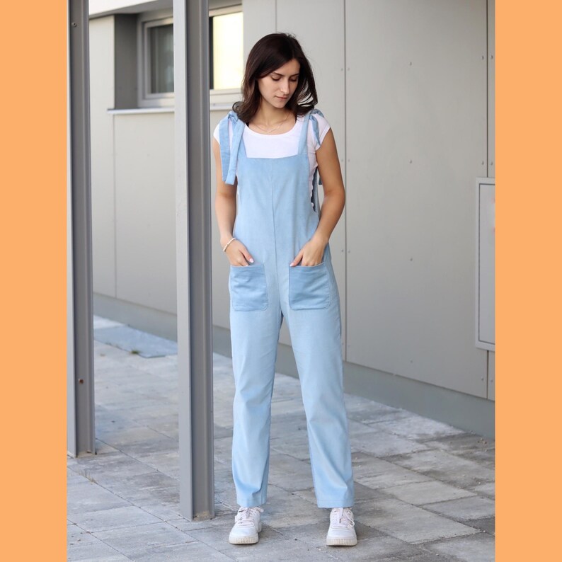 May include: A light blue denim overall with adjustable straps and two front pockets. The overall is worn by a person with long brown hair.