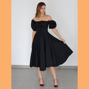 May include: A black off-the-shoulder dress with short, puffed sleeves and a full skirt. The dress is paired with burgundy heels. The dress has a fitted bodice and a flared skirt, creating a classic silhouette. The dress is knee-length.