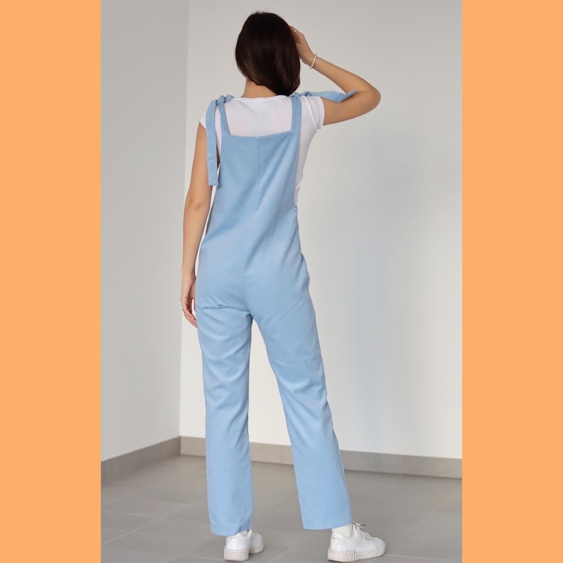 May include: A light blue overall jumpsuit with thin straps that tie at the shoulders. The straps are made of the same fabric as the jumpsuit. The jumpsuit has a relaxed fit and straight legs.