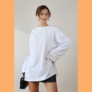 May include: A white long-sleeved oversized t-shirt with a relaxed fit. The shirt is made of a soft, comfortable fabric and has a crew neckline.
