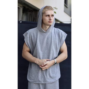 May include: A sleeveless gray hoodie and matching sweatpants. The hoodie has a hood and a relaxed fit. The outfit is made of a soft, comfortable material. The person is wearing a silver watch.