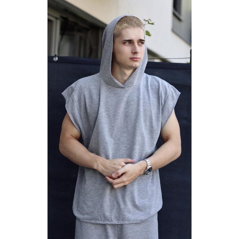 May include: A sleeveless gray hoodie and matching sweatpants. The hoodie has a hood and a relaxed fit. The outfit is made of a soft, comfortable material. The person is wearing a silver watch.