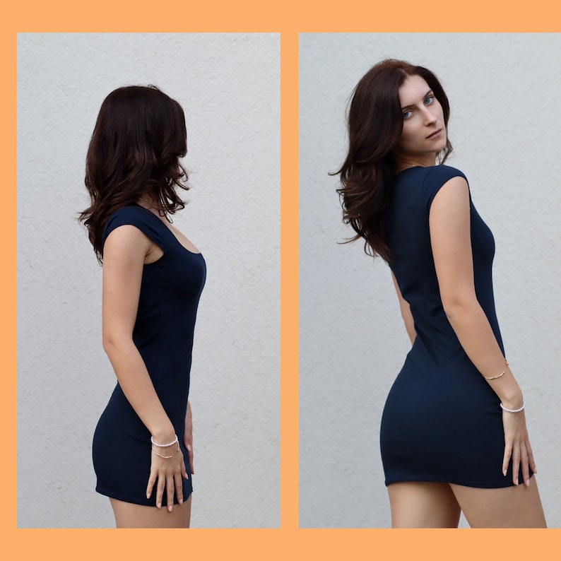 May include: A woman wearing a dark blue sleeveless dress. The dress is fitted and has a scoop neckline. The woman is standing in front of a white wall.