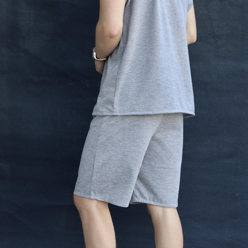 May include: A gray sleeveless shirt and matching shorts set. The casual outfit is made of a soft, knit fabric. The shorts are knee-length. The person is wearing a silver bracelet.