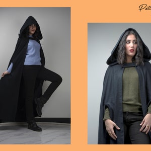 May include: Two women wearing black hooded capes. The cape has a long, flowing design and is made of a soft, drapey fabric. The women are wearing different coloured sweaters underneath the capes.