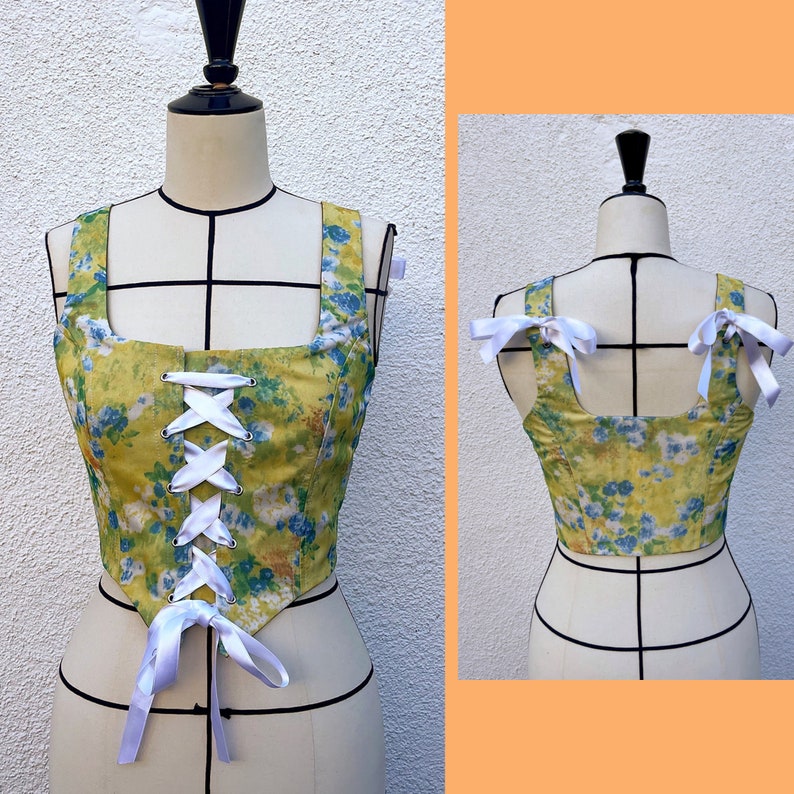 May include: A yellow and blue floral print corset top with white ribbon lacing and bow details. The top has a square neckline and sleeveless design.