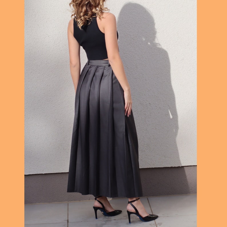 May include: A long, black, pleated skirt with a high waist. The skirt is made of a smooth, silky fabric.