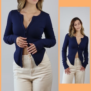 May include: A navy blue long-sleeved shirt with a front zipper. The shirt is fitted and has a ribbed texture. The model is wearing the shirt with beige pants.