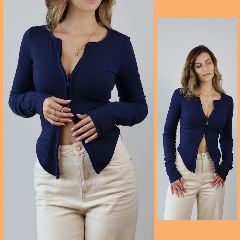 May include: A navy blue long-sleeved shirt with a front zipper. The shirt is fitted and has a ribbed texture. The model is wearing the shirt with beige pants.