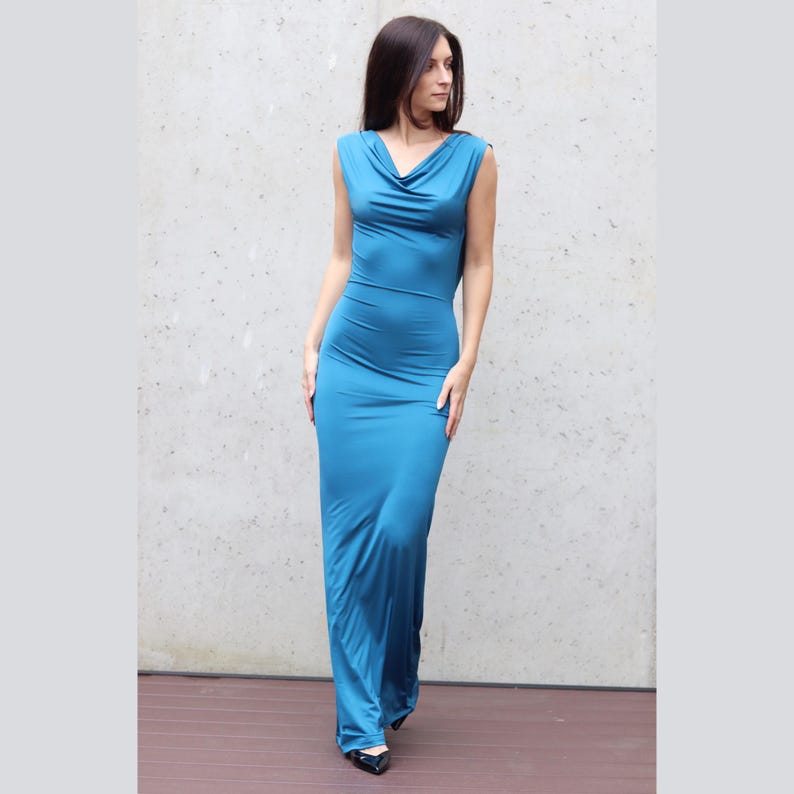 Puede incluir: Un vestido largo sin mangas, color teal, con cuello de cisne. El vestido es entallado, acentuando la silueta. La tela parece suave y fluida. La persona lleva zapatos negros.
