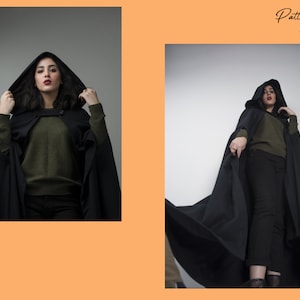 May include: A woman wearing a black hooded cape with a green sweater and black trousers. The cape is long and flowing, and the woman is standing in a studio setting.