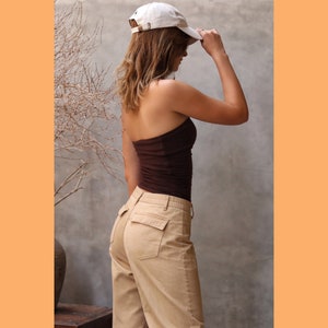 May include: A woman wearing a brown tube top and beige cargo pants. She is wearing a white baseball cap and has her hair pulled back.