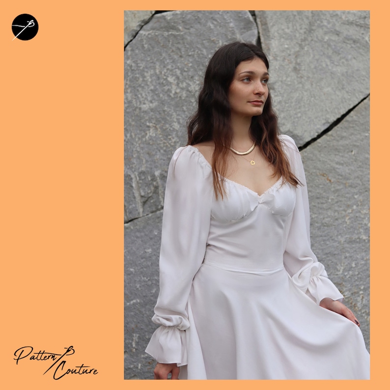 May include: A white dress with long sleeves and a sweetheart neckline. The dress has a ruffled trim around the neckline and cuffs. The model is wearing a gold necklace.