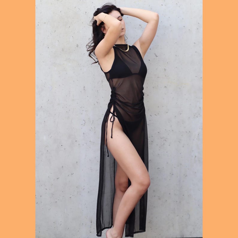 May include: A black sheer maxi dress with a high neckline and side slits. The dress is made from a lightweight, flowing fabric and has a drawstring at the waist.