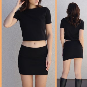 May include: A black crop top with short sleeves and a black mini skirt. The outfit is made of a stretchy fabric.
