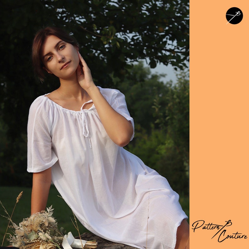 May include: A woman wearing a white, loose-fitting dress with a gathered neckline and short sleeves. She is sitting on a log in a grassy area with a bouquet of dried flowers in her lap. The background is a blurred image of trees.
