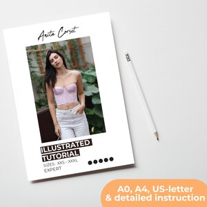 K&ouml;nnte beinhalten: Ein wei&szlig;es Papier mit dem Text "Anita Corset" und "ILLUSTRATED TUTORIAL" wird angezeigt. Das Tutorial umfasst die Gr&ouml;&szlig;en XXS-XXXL. Das Bild auf dem Papier zeigt eine Person, die ein rosa Korsett und eine wei&szlig;e Hose tr&auml;gt. Ein wei&szlig;er Bleistift befindet sich rechts.
