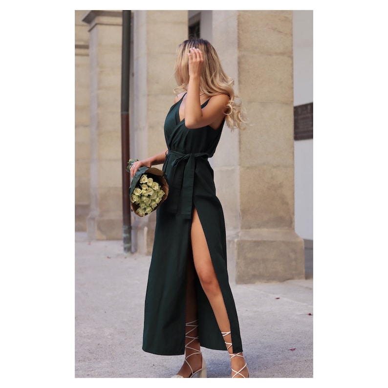 Puede incluir: Una mujer con un vestido maxi verde oscuro con una abertura lateral y un cintur&oacute;n a juego. Lleva un ramo de rosas blancas.