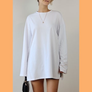 May include: A white long-sleeved t-shirt with a relaxed fit. The shirt has a crew neckline and a simple design.
