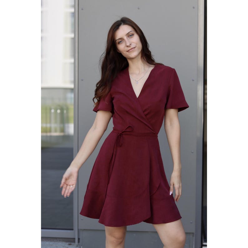 Peut inclure: Une robe portefeuille bordeaux &agrave; manches courtes et col en V. La robe est dot&eacute;e d'une ceinture &agrave; la taille et d'une jupe &eacute;vas&eacute;e. Le tissu semble &ecirc;tre une mati&egrave;re douce et fluide.