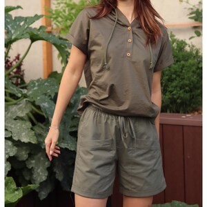 May include: A green hooded shirt and matching shorts set. The shirt has a button placket and a drawstring hood. The shorts have a drawstring waist and two pockets.