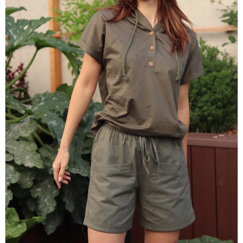 May include: A green hooded shirt and matching shorts set. The shirt has a button placket and a drawstring hood. The shorts have a drawstring waist and two pockets.