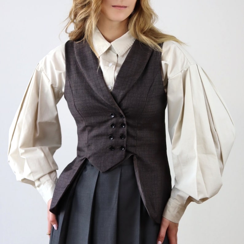 May include: A brown patterned waistcoat with a notched collar and a double-breasted fastening. The waistcoat has a fitted silhouette and a pointed hem. The waistcoat is worn over a white button-down shirt with puffed sleeves.