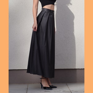 May include: A black maxi skirt with a high waist and pleats. The skirt is made of a smooth, silky fabric.