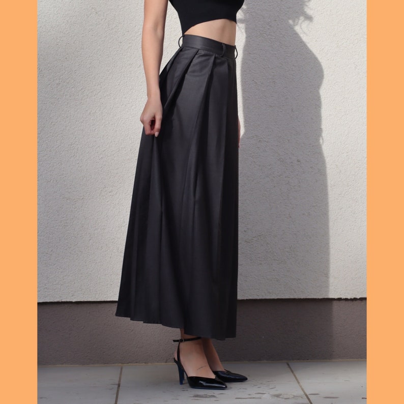 May include: A black maxi skirt with a high waist and pleats. The skirt is made of a smooth, silky fabric.