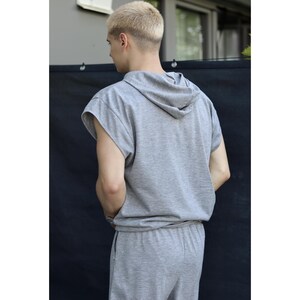 May include: A gray sleeveless hoodie and matching sweatpants. The hoodie has a drawstring hood and a relaxed fit. The sweatpants have an elastic waistband. The outfit is made of a soft, comfortable material. The person is facing away from the camera.