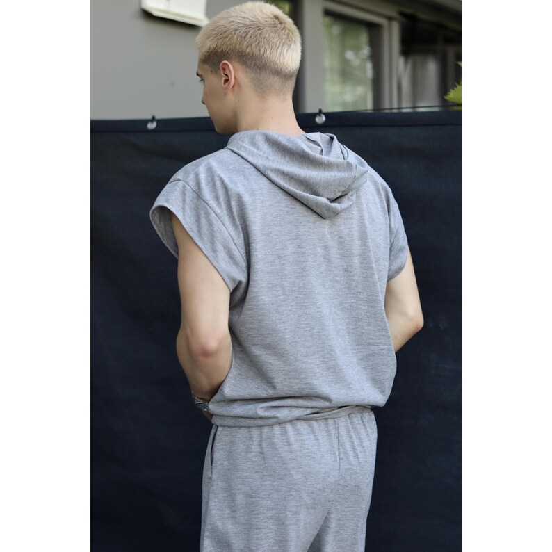 May include: A gray sleeveless hoodie and matching sweatpants. The hoodie has a drawstring hood and a relaxed fit. The sweatpants have an elastic waistband. The outfit is made of a soft, comfortable material. The person is facing away from the camera.