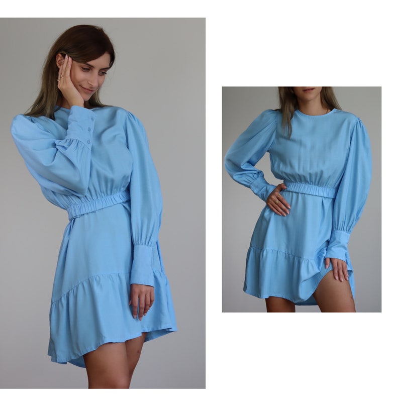 Puede incluir: Un vestido azul claro con mangas largas, cuello redondo y cintura ajustada. El vestido tiene un dobladillo con volantes y una falda fruncida.