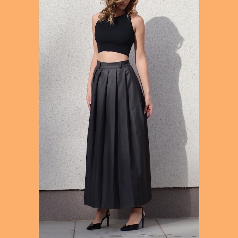 May include: A black, pleated maxi skirt with a high waist. The skirt is made of a smooth, silky fabric and falls to the ankles.
