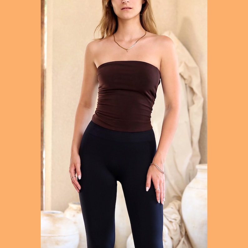 May include: A woman wearing a brown tube top and black leggings. The top is a simple, fitted style with no straps. The leggings are a solid black color and fit snugly.