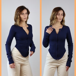 May include: A navy blue long-sleeved shirt with a zipper closure. The shirt has a fitted silhouette and a ribbed texture. The model is wearing the shirt with beige pants.