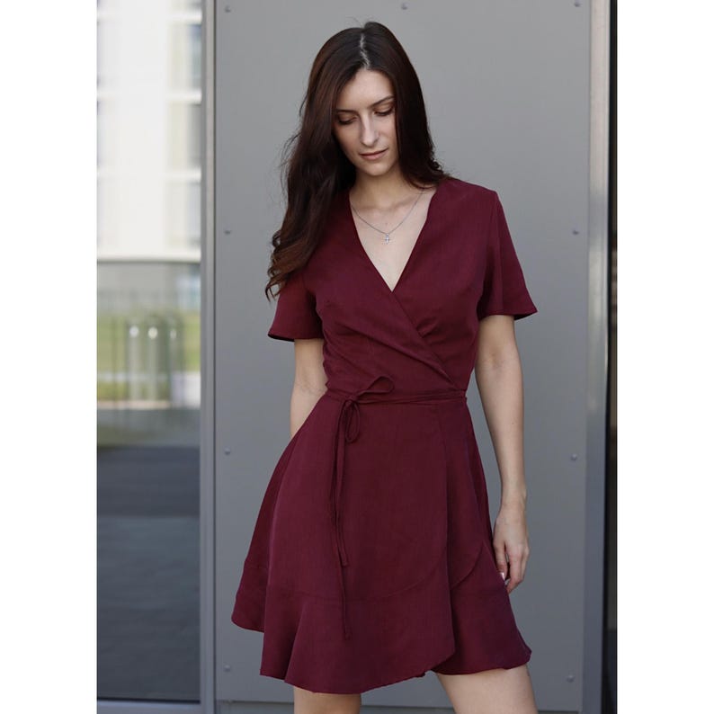 Peut inclure: Une robe portefeuille bordeaux &agrave; manches courtes et col en V. La robe est dot&eacute;e d'une taille nou&eacute;e et d'une jupe &eacute;vas&eacute;e avec un ourlet &agrave; volants. Le tissu semble &ecirc;tre l&eacute;ger, adapt&eacute; aux temp&eacute;ratures chaudes.