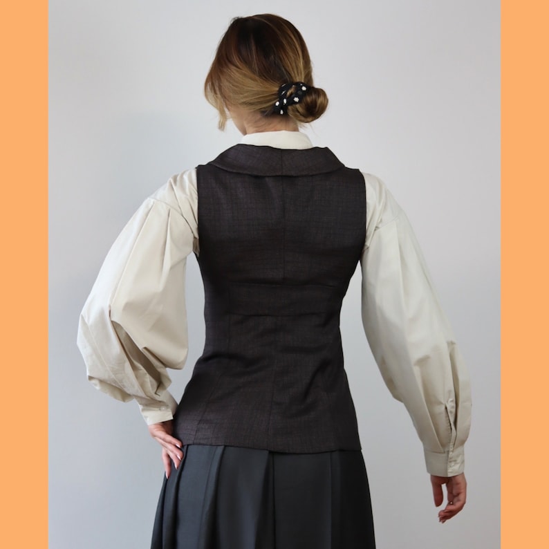 May include: A brown waistcoat with a white blouse underneath. The waistcoat has a classic, tailored fit and a slightly cropped length. The blouse has long, puffed sleeves and a simple, collared neckline.