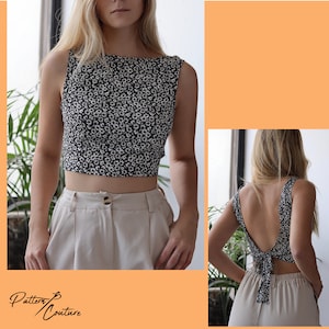 Op de afbeelding: Een zwart-wit bloemen crop top met een strikdetail op de rug. De top is mouwloos en heeft een ronde hals. Het model draagt de top met een beige broek.