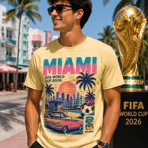 May include: A light yellow t-shirt with a graphic design featuring the word "MIAMI" in blue and pink, palm trees, a sunset, and a vintage car. The text "FIFA WORLD CUP 2026" is also displayed.