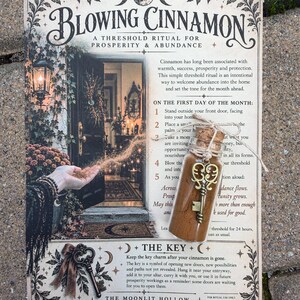 May include: A printed instructional card titled Blowing Cinnamon featuring a ritual guide for prosperity and abundance, accompanied by a small glass vial filled with ground cinnamon, sealed with a cork, and adorned with a decorative brass key charm.