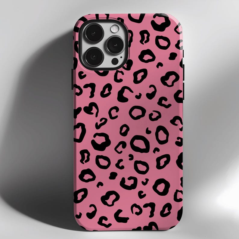 May include: A pink phone case with a black leopard print design. The case has a cutout for the camera lens.