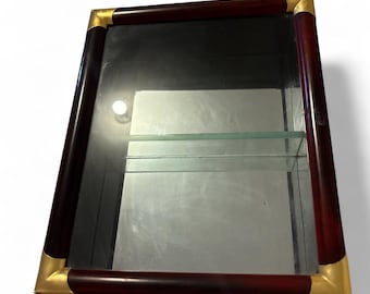 May include: A rectangular display cabinet with a dark wood frame and brass corner accents. The cabinet has a mirrored back and glass shelves. The frame is a rich, dark brown color, and the brass corners add a touch of elegance.