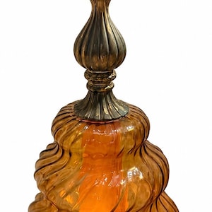 May include: A table lamp featuring a translucent amber glass base with a swirling, ribbed texture. The lamp has an ornate, antique-style brass metal base and a matching brass neck section. A single light bulb is visible at the top of the fixture.