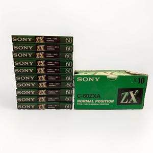 Puede incluir: Una pila de diez casetes de audio Sony ZX C-60 verdes junto a su caja de cartón verde original. Cada casete está etiquetado como Type I IEC I Normal 60. La caja está marcada con Sony C-60ZXA Normal Position Type I IEC I Normal Position x10.