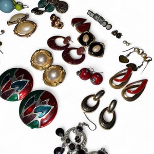 Könnte beinhalten: Eine Sammlung von Vintage-Ohrringen in verschiedenen Stilen und Farben. Enthält goldfarbene, Perlen- und Emaille-Ohrringe. Einige sind Clip-Ons, andere haben Stifte oder Haken. Die Ohrringe sind auf einer weißen Oberfläche angeordnet.
