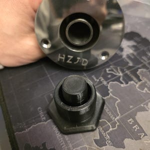 以下が含まれることがあります： 3つの穴と「HZJD」の文字が刻まれた、光沢のあるステンレス鋼の部品。黒い六角形のオブジェクトが近くにあります。オブジェクトは地図をテーマにした表面にあります。