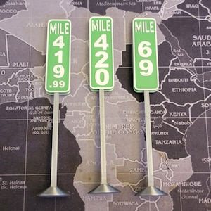 Könnte beinhalten: Drei grüne und weiße Meilensteine mit schwarzem Text. Die Schilder zeigen "Mile 419.99", "Mile 420" und "Mile 69".