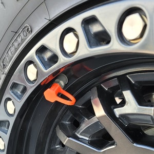 May include: Close-up of a black tire with a silver rim and a bright orange valve stem cap. The tire has the text "M/T F2220" printed on the side.